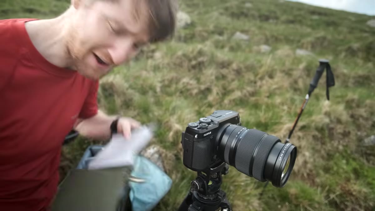 Camera mounted on tripod pointed at cone-shaped mountain peak