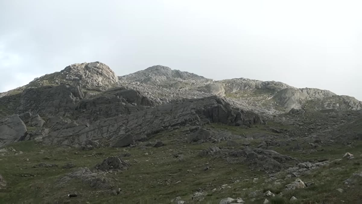 Wide shot of mountain campsite location with tarn visible in background