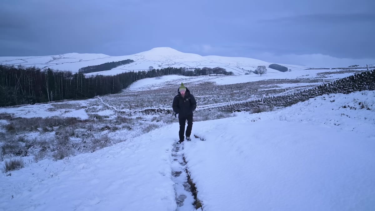 Danson walking through snowy Peak District hillside in layered gear