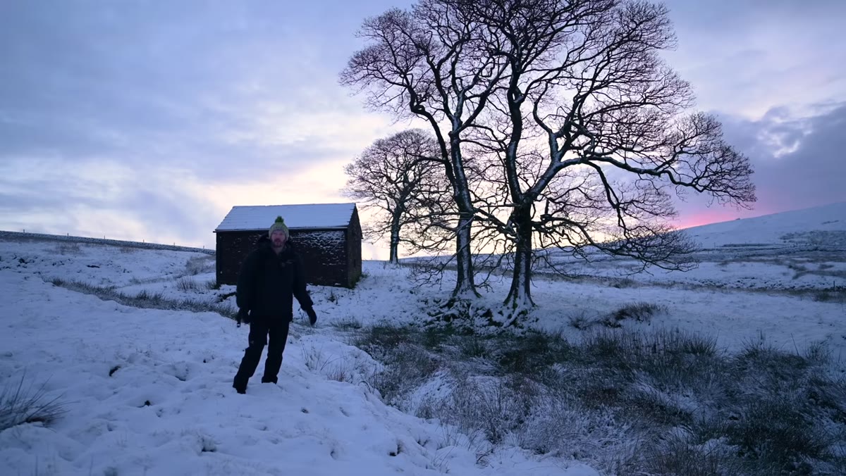 Danson approaching stone barn in snowy field, assessing scene
