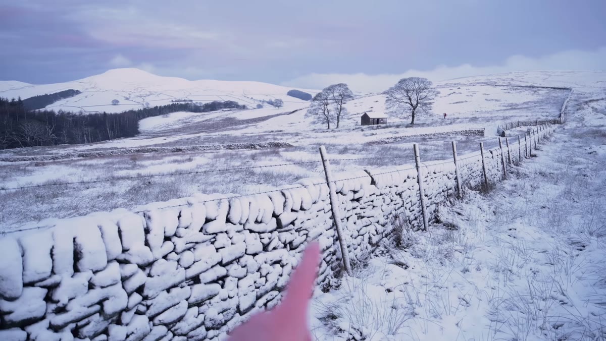Stone wall line extending into snowy landscape toward background hill