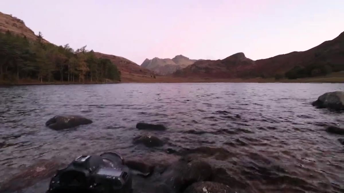 Wide shot of tarn with stones in foreground, mountains and sky beyond