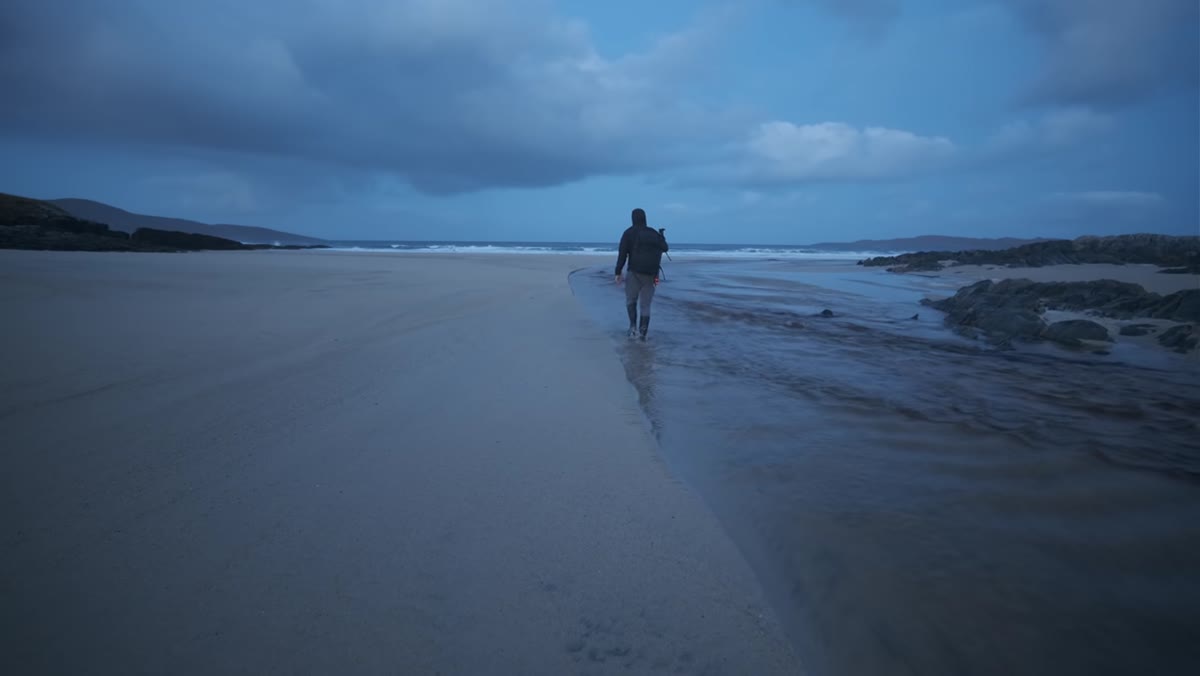 Photographer wading through river to reach pristine beach