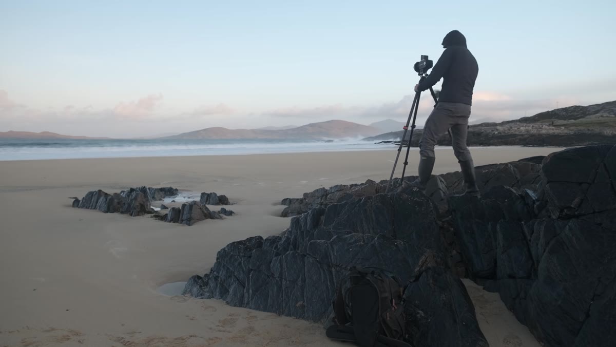 Photographer repositioning repeatedly to align foreground rocks with distant island