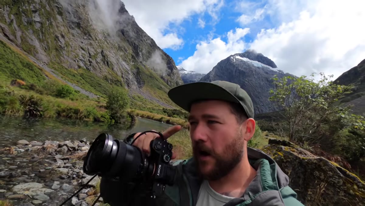Photographer gesturing toward a mountain peak behind him in the valley