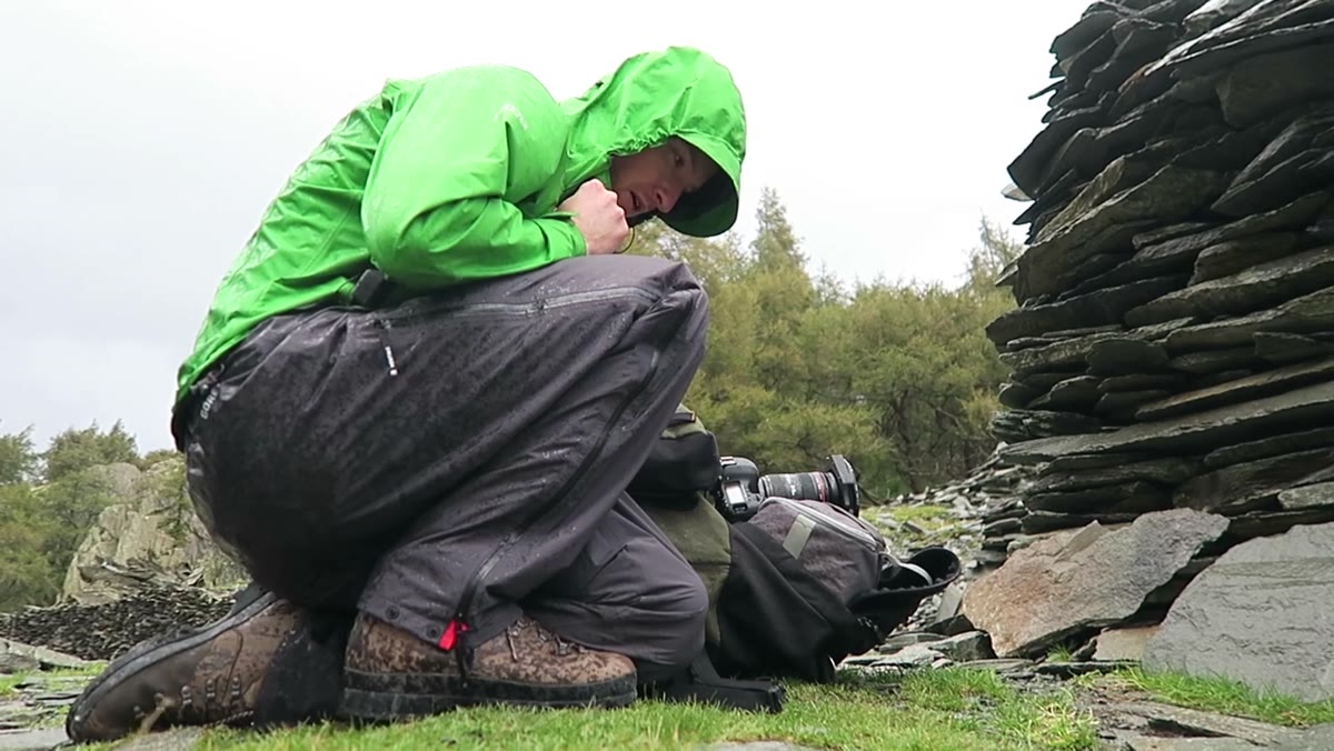Heaton crouching to shelter camera during heavy rain shower