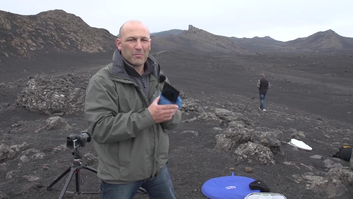 Karl Taylor standing in volcanic landscape, camera lowered, surveying the scene