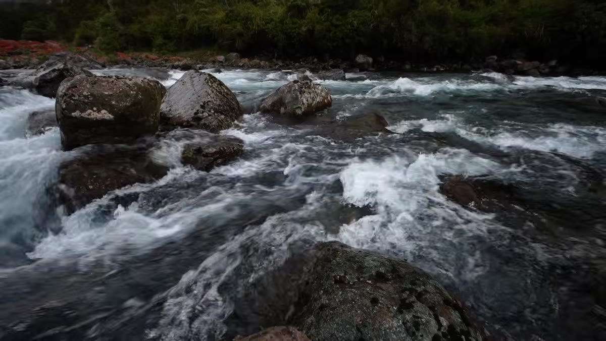 Photographer examining river cascade and rocks at water&rsquo;s edge