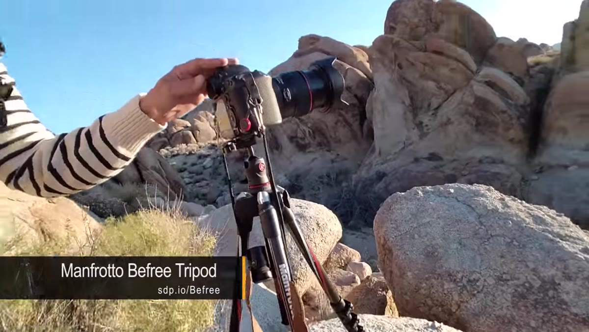 Lightweight tripod visibly shaking in wind, photographer steadying it by hand