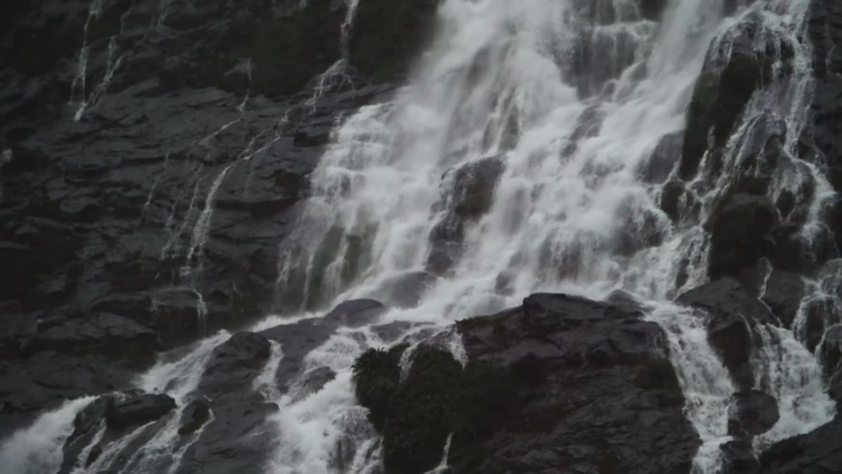 Telephoto lens compressing rain-soaked cliffs and waterfall distance