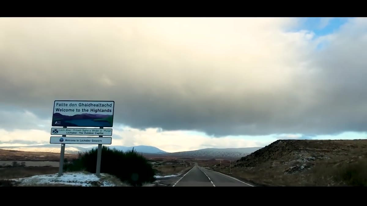 Photographer paused roadside with Scottish mountain behind him