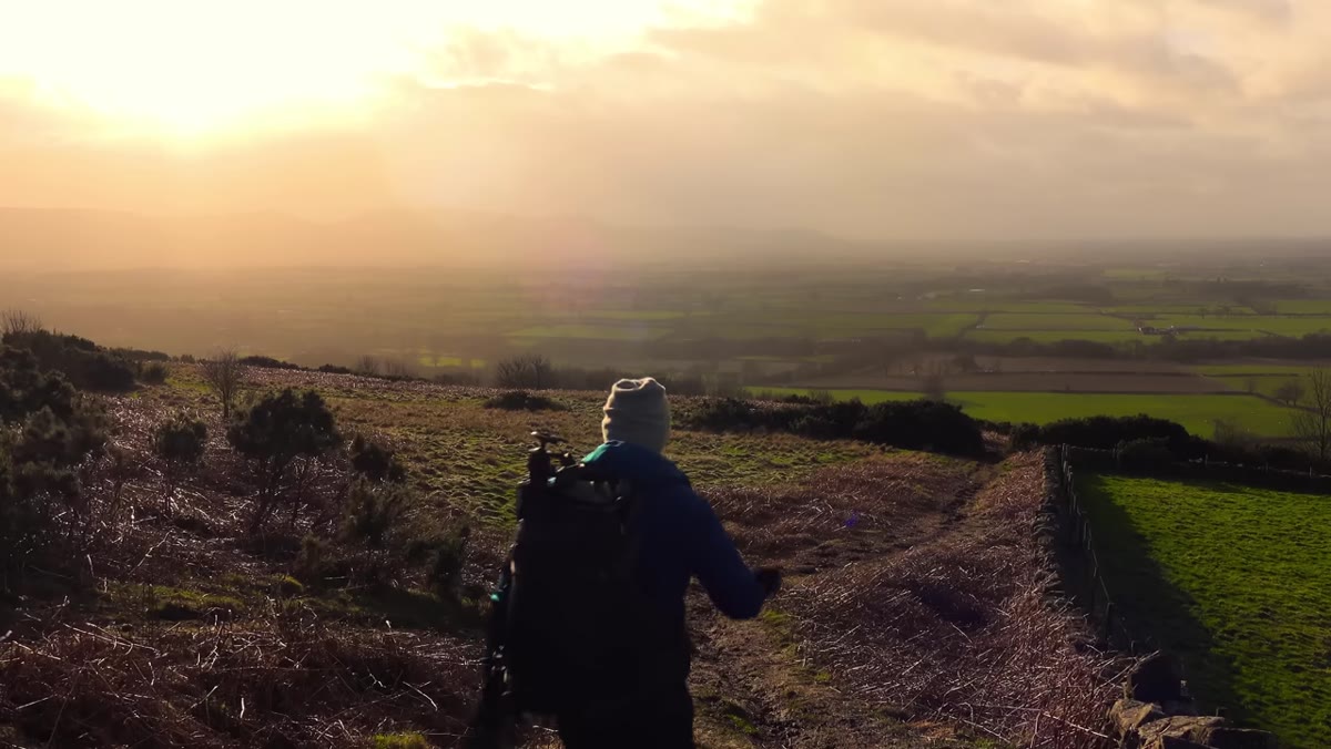 Photographer walking downhill toward wooded valley
