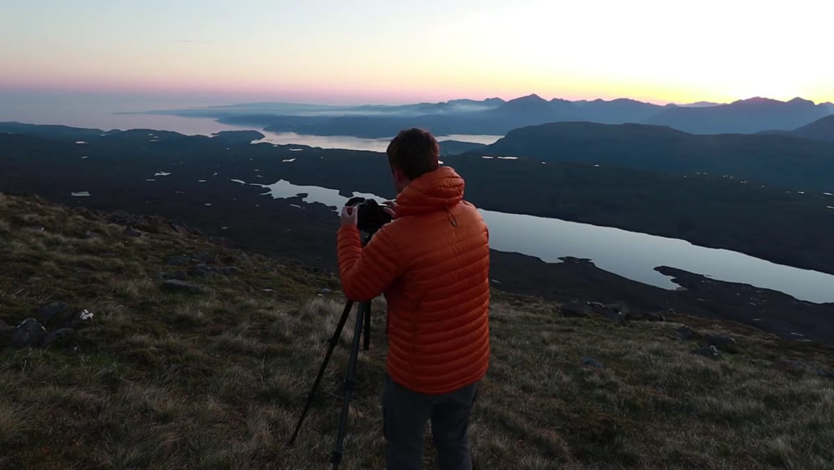 Camera set up on tripod pointing toward still lochs at sunrise