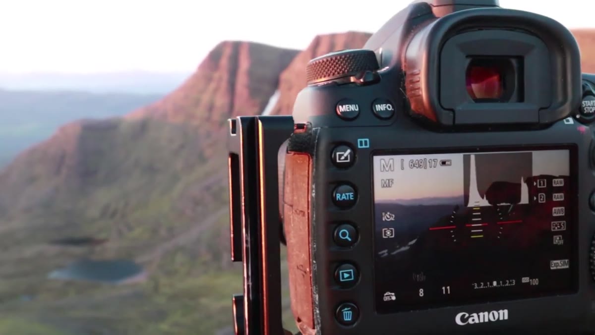 Camera set up on tripod aimed at lit rock buttress in morning light