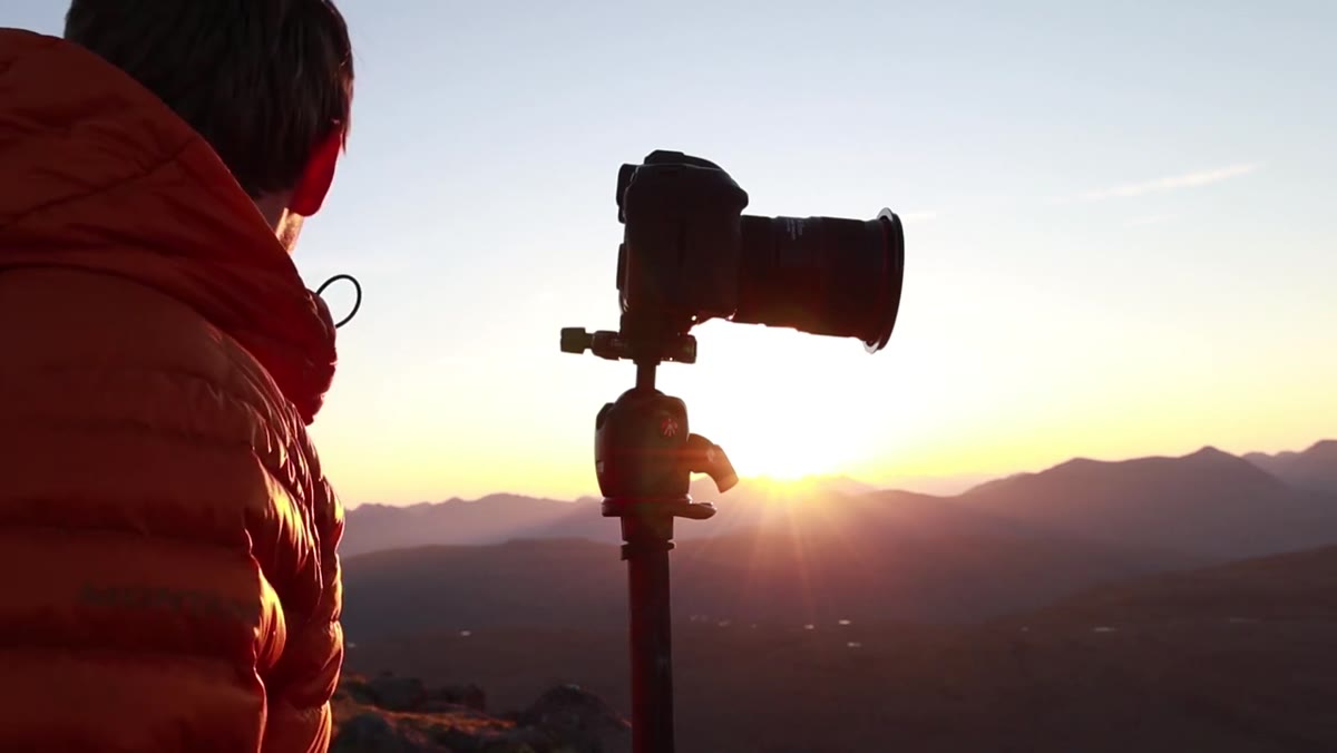 Photographer lowering camera as sun fully rises over landscape