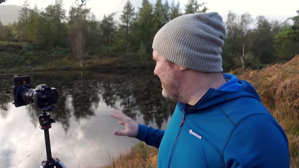 Adam standing beside a small pond looking toward sunlit trees