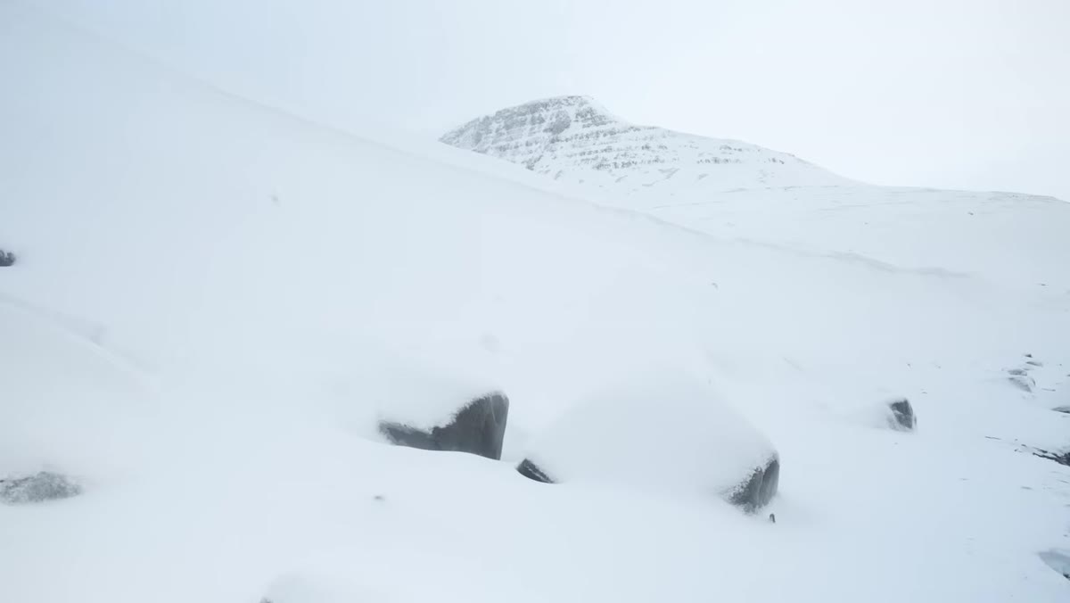 Boulders emerging from snow with mountain backdrop, minimal elements