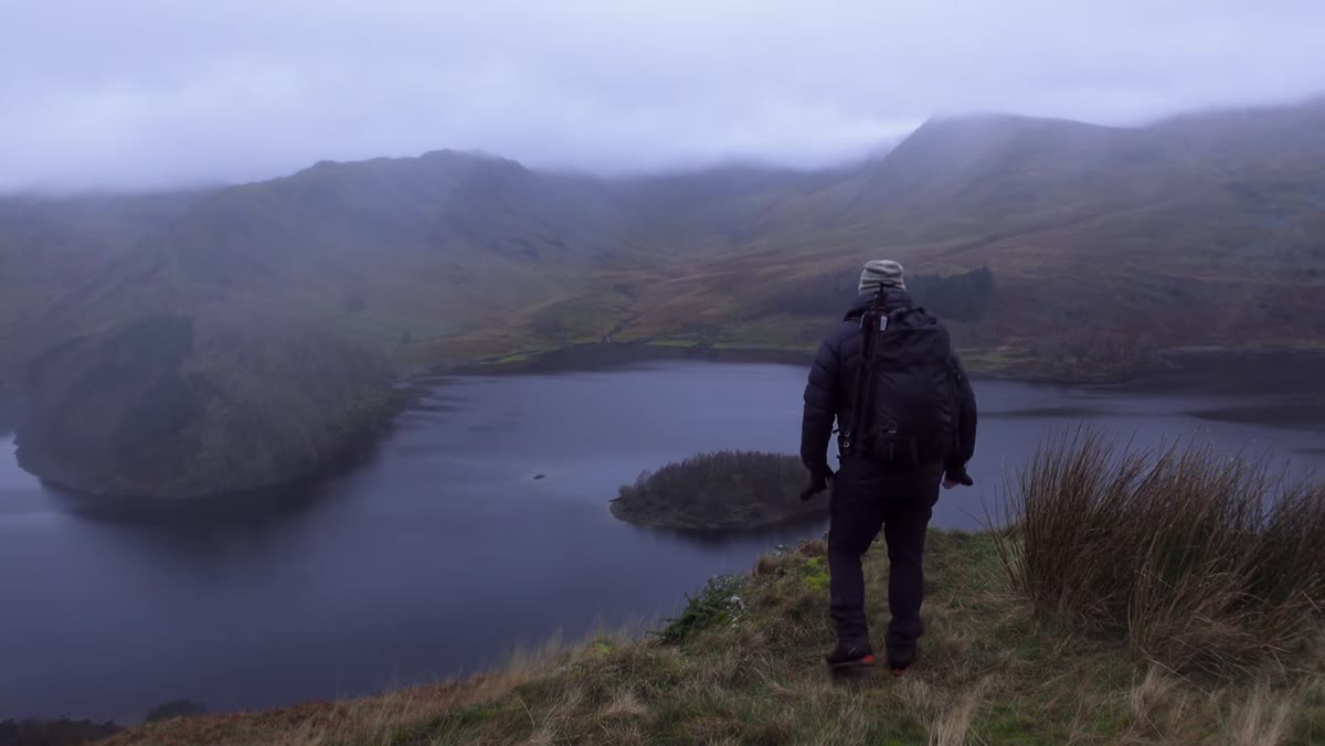 Adam hiking uphill in overcast misty conditions, mountains visible behind
