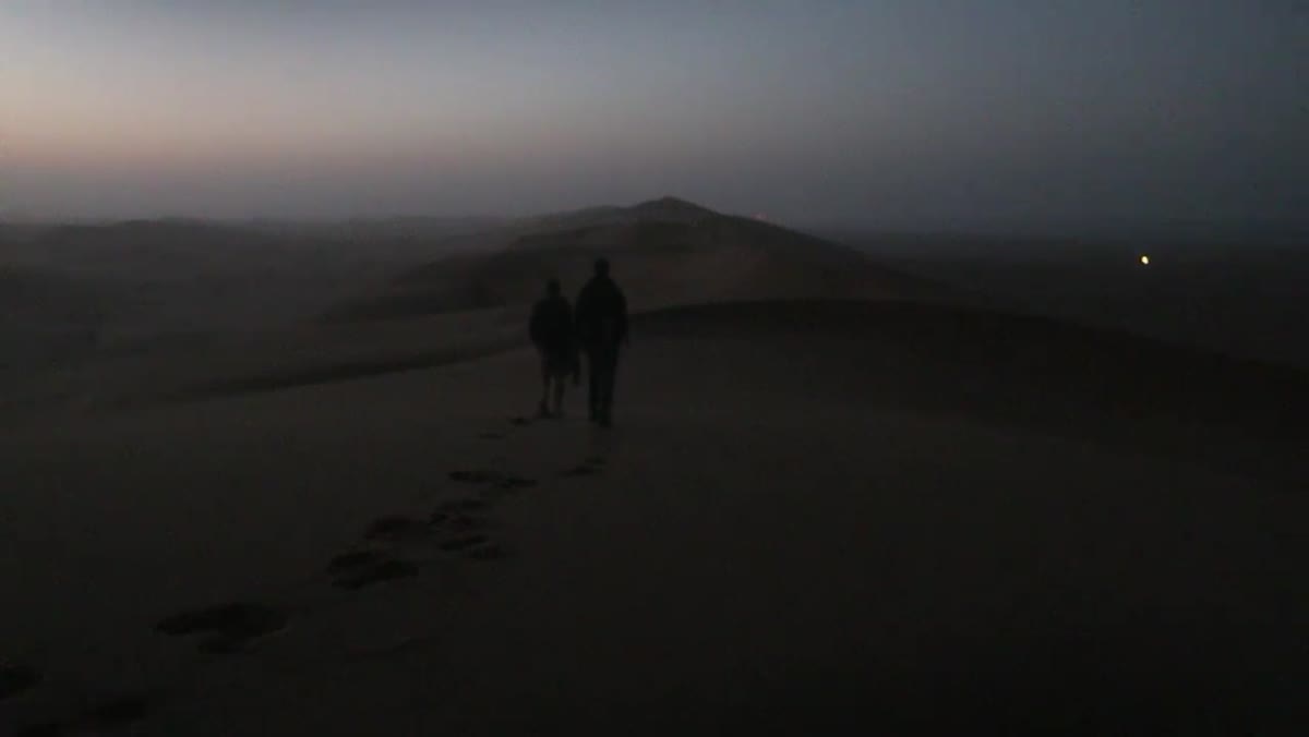 Photographer walking through white dunes in dim pre-sunrise light