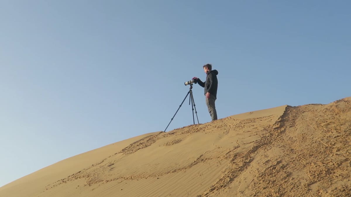 Photographer with long lens raised, shooting across dune landscape